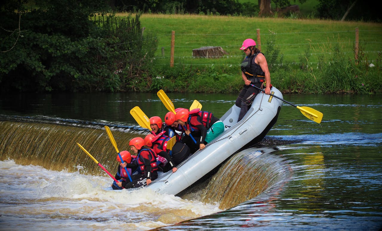about-us Adventurous group whitewater rafting at Llangollen, Wales, going over a small waterfall.