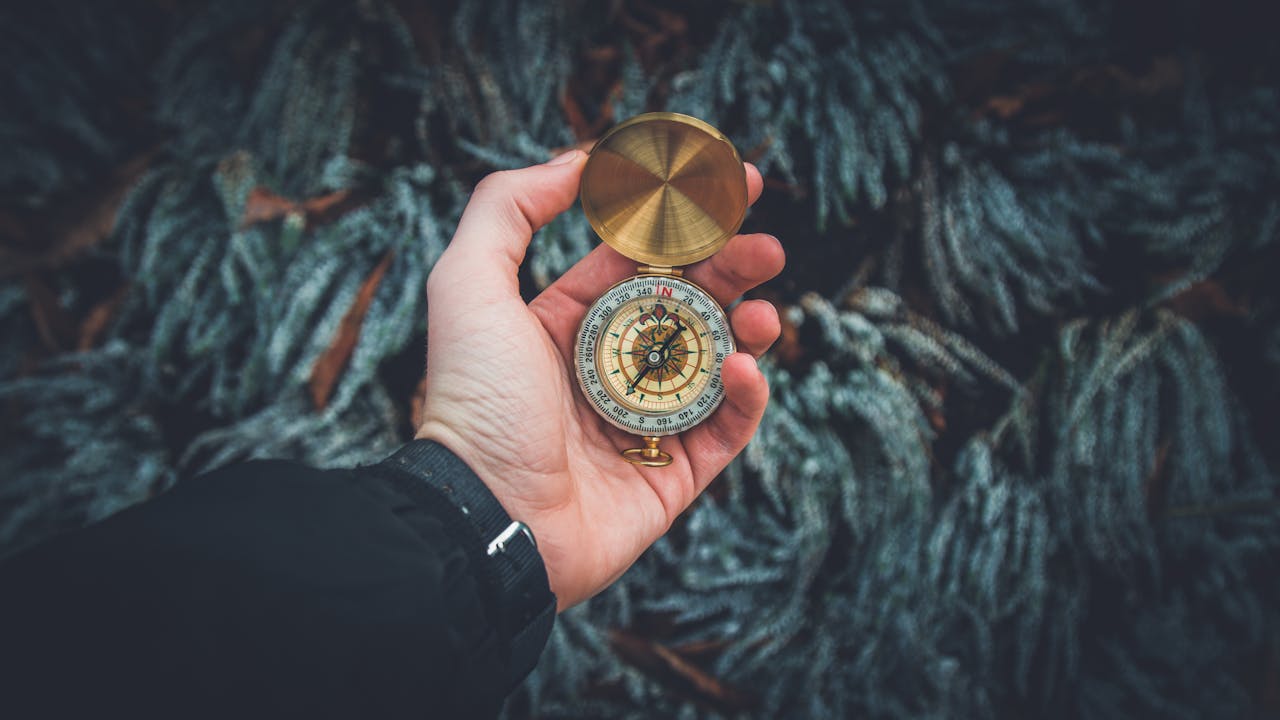 who-we-are A close-up shot of a hand holding a vintage compass against a natural background.